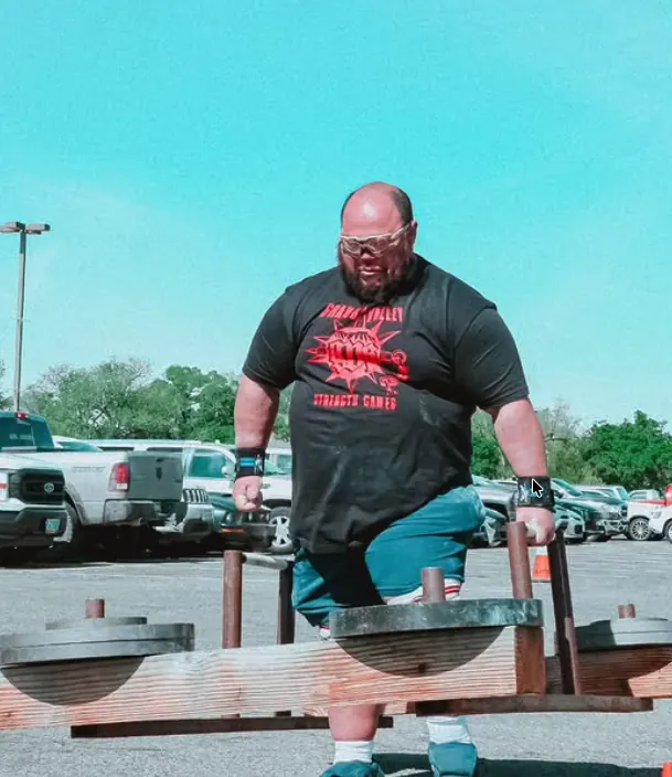 Strongman athlete carrying heavy implements outdoors